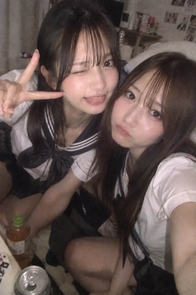 低画質のiPhoneで撮影したような写真。セーラー服姿の20歳の日本人女性が友人の家で友人と自撮りしている。