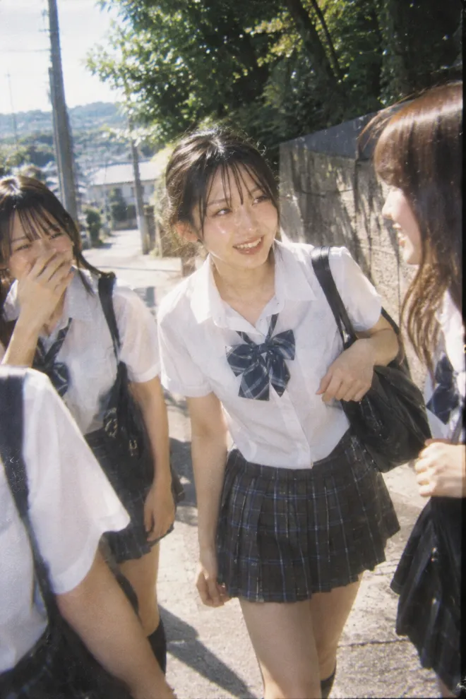 使い捨てカメラで撮ったようなラフなスナップ。制服姿の20歳の日本人女性が夏の通学路で複数の友人と話している。