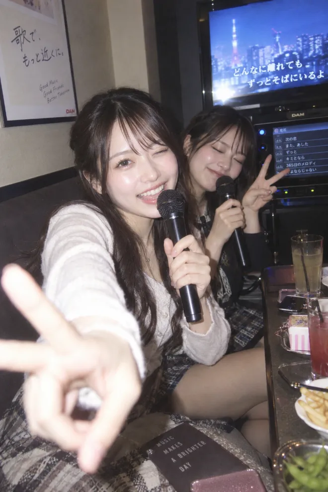 CCDカメラで撮影したような柔らかなポートレート。フェミニン系ファッションの20歳の日本人女性が友人とカラオケを楽しんでいる。