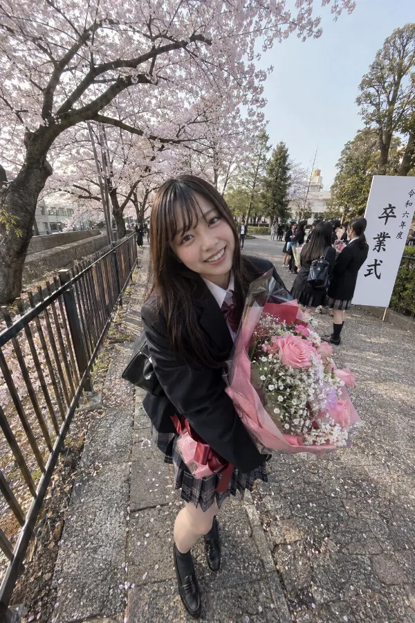 卒業式の桜並木。花束を持つ制服姿の日本人女性と満開の桜の写真。