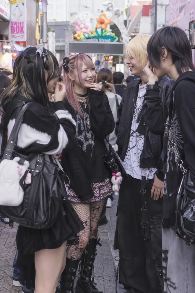 ストリートフォトグラフィー風。原宿系ファッションの20歳の日本人女性が複数の友人と会話している。