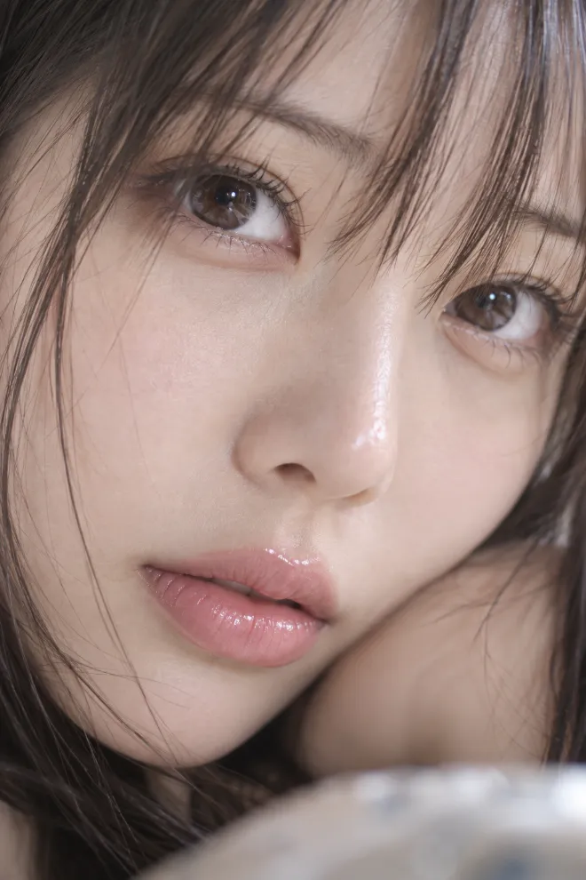 マクロ撮影による顔のクローズアップ。20歳の日本人女性の長いまつ毛、瞳、鼻、唇、リップグロスを細部まで捉え、背景はごくわずかに抽象化されている。