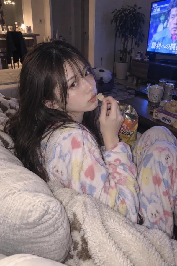 夜のリビング。ソファ、毛布、テレビの光、スナックが並ぶくつろぎの風景。